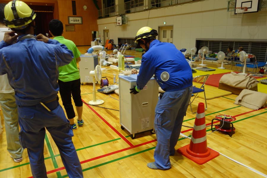 避難所となった野村中学校体育館でのスポットクーラー設置作業（１１日、四国電力提供）