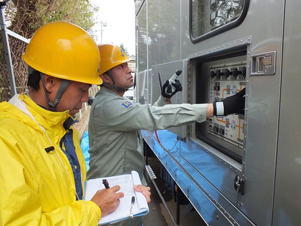 停電が長引く八街市の川上小学校には15日から、沖縄電力からの応援部隊が発電機車で電力供給を開始した。これにより川上小学校は17日から授業を再開。鈴木浩明校長は「最初に沖縄電力の車を見た時は、そんな遠くからと驚いた。地域は停電中なので頂いた電気を大事に使っている。感謝してもしきれない」と話した（写真は18日、発電機車の状態をチェックする沖縄電力の応援隊）。隣の学校には東北電力の応援隊が発電機車で電気を供給していた 